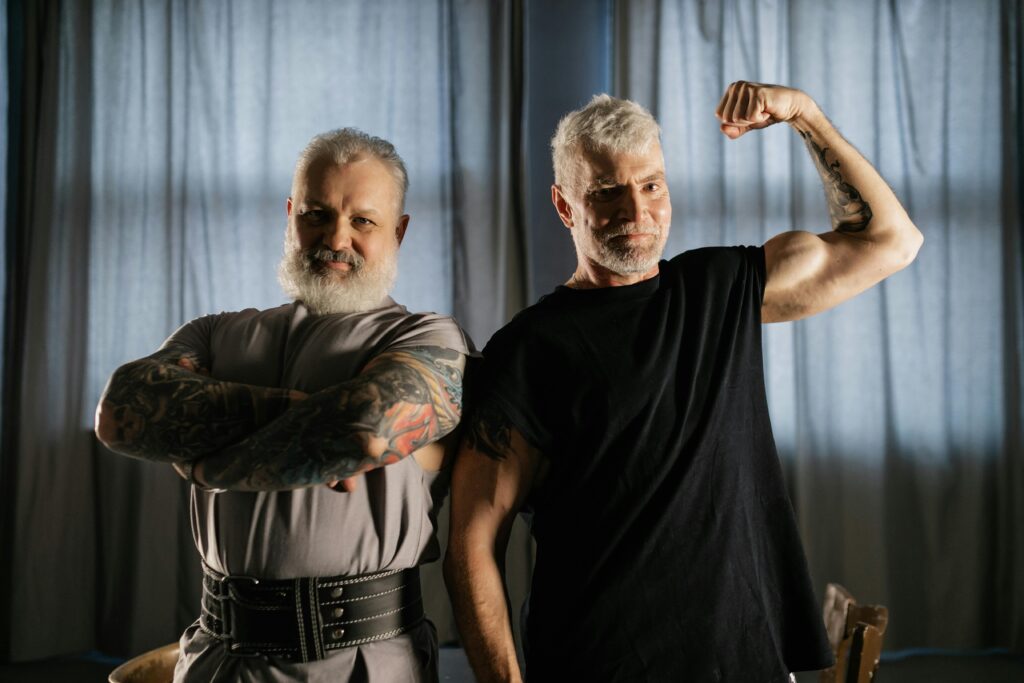 Two older men flexing muscles after exercise, symbolizing strength, longevity, and healthy aging.